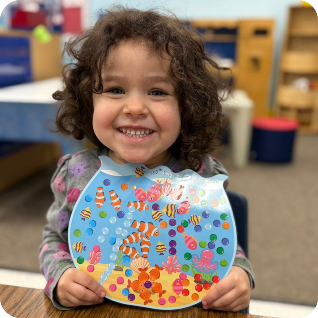 Smiling preschool girl holding art project at Gloryland Preschool in Grayslake, Illinois